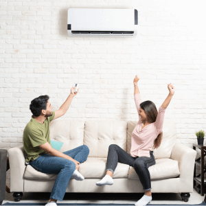 Couple Sitting Below Mini Split On Sofa At Home