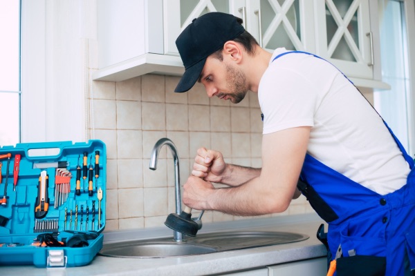 plumber cleaning clogged drain in kitchen sink with plunger