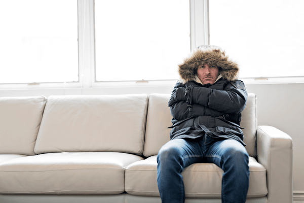 winter furnace troubleshooting- man in coat on couch- not heat cold inside